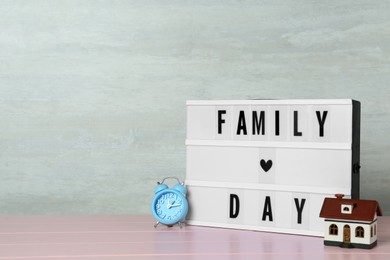 Photo of Lightbox with text Family Day, house model and alarm clock on pink wooden table. Space for design