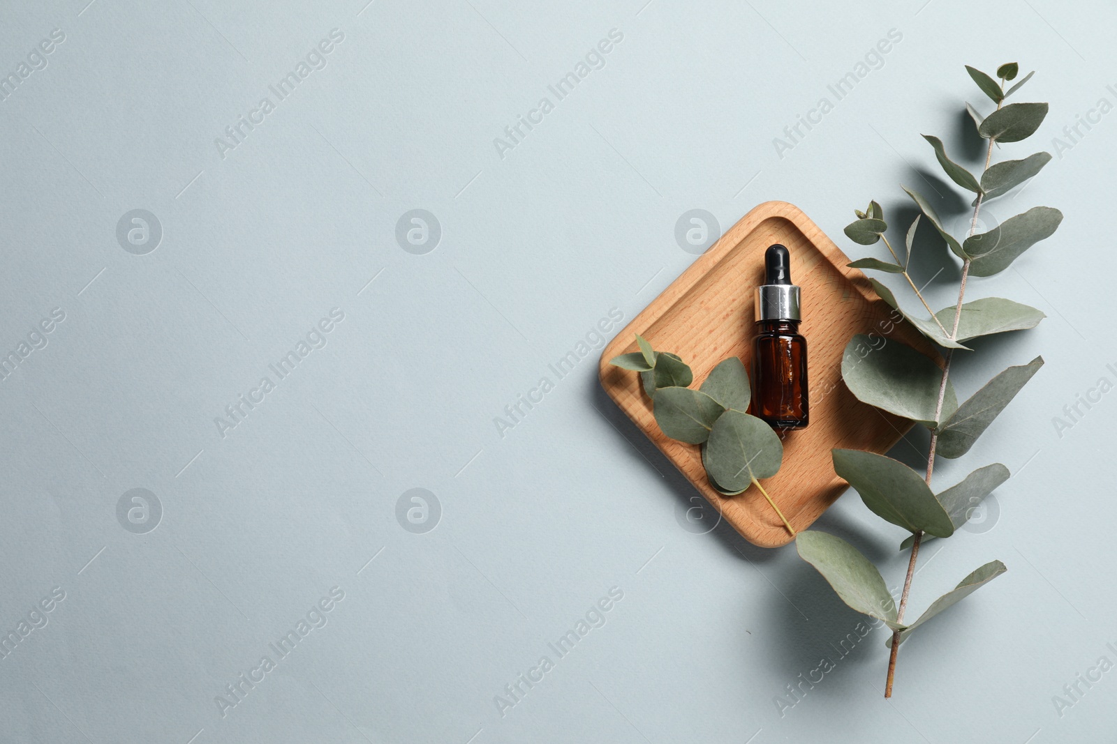 Photo of Aromatherapy product. Bottle of essential oil and eucalyptus branches on grey background, flat lay. Space for text