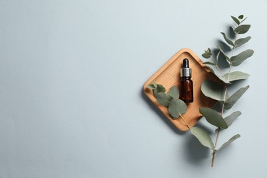 Aromatherapy product. Bottle of essential oil and eucalyptus branches on grey background, flat lay. Space for text