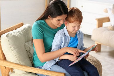 Photo of Mother reading book with her son on armchair in living room at home