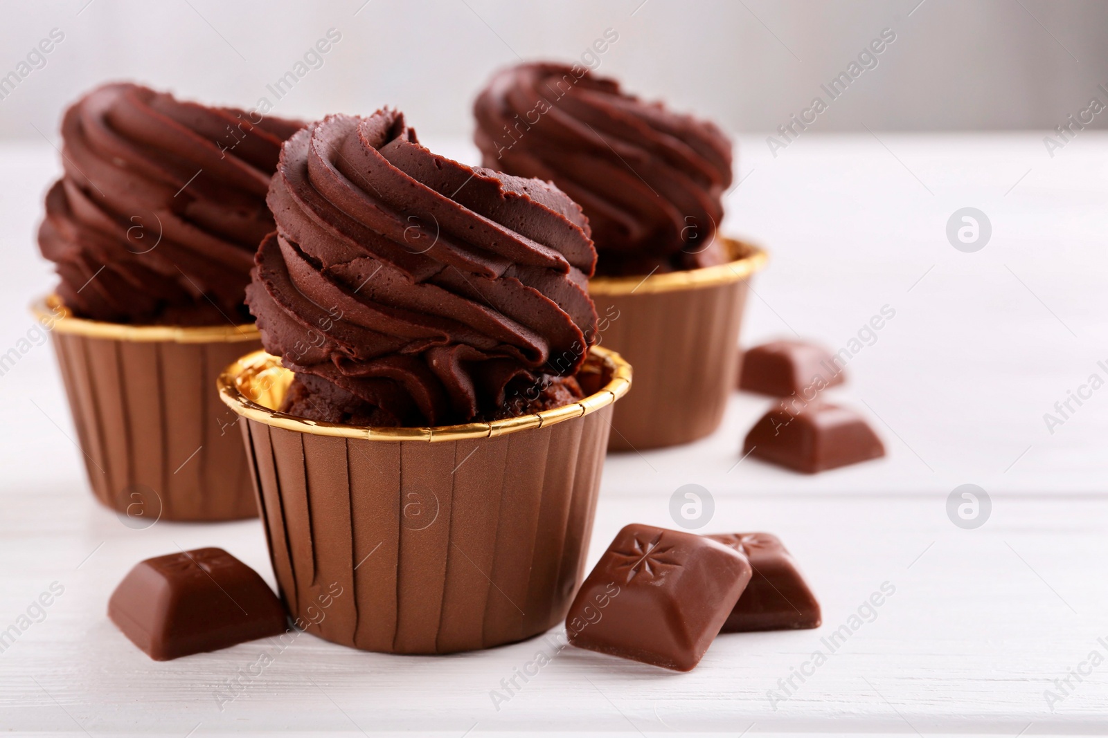 Photo of Delicious cupcakes and chocolate pieces on white wooden table, closeup