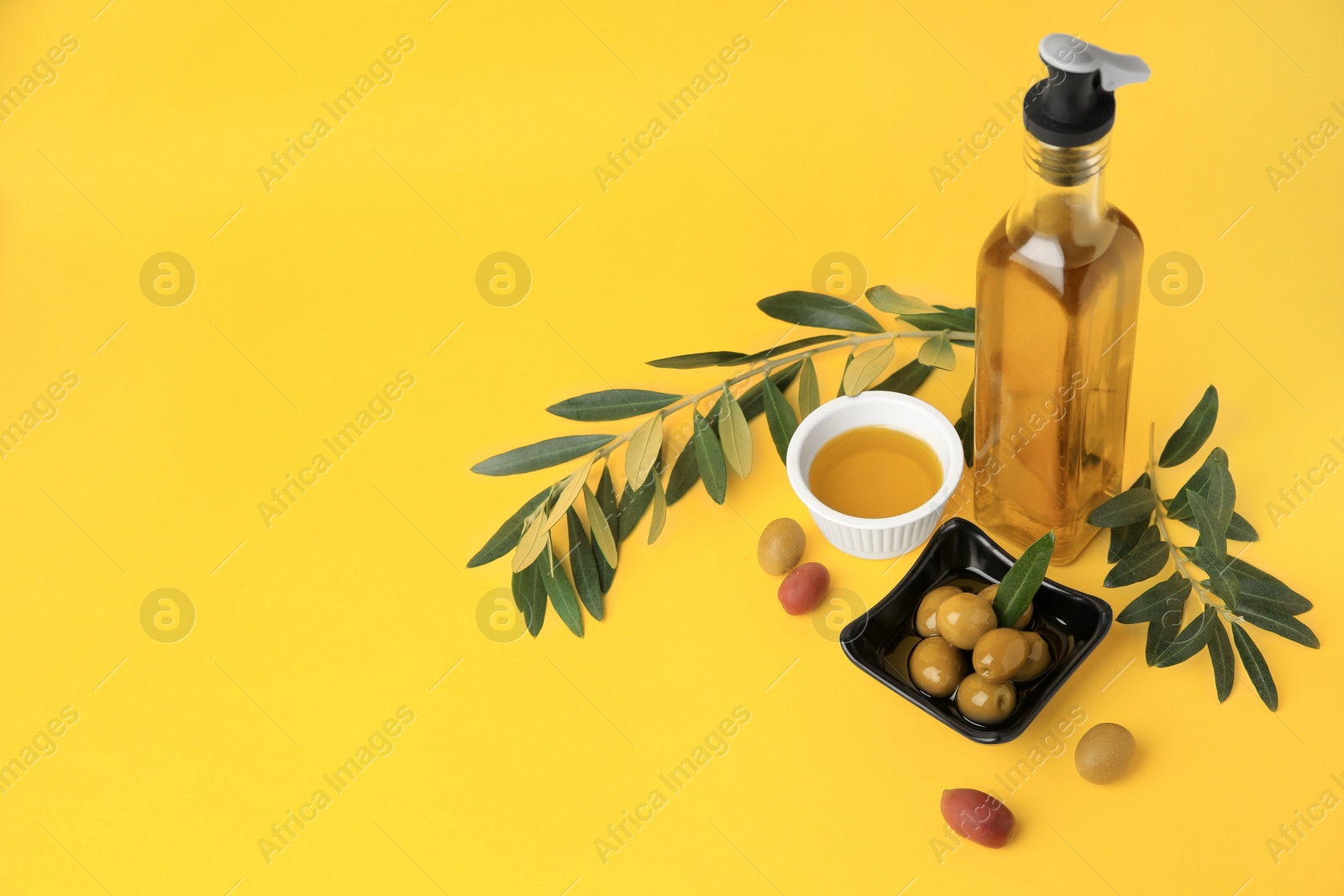 Photo of Oil, olives and tree twigs on yellow background, space for text