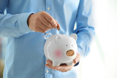 Photo of Man putting coin into piggy bank, closeup. Money savings