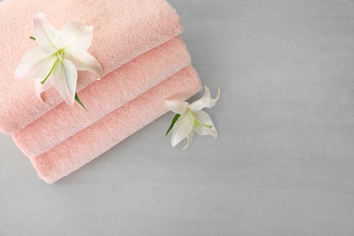 Stack of fresh towels with flowers on grey table, top view. Space for text