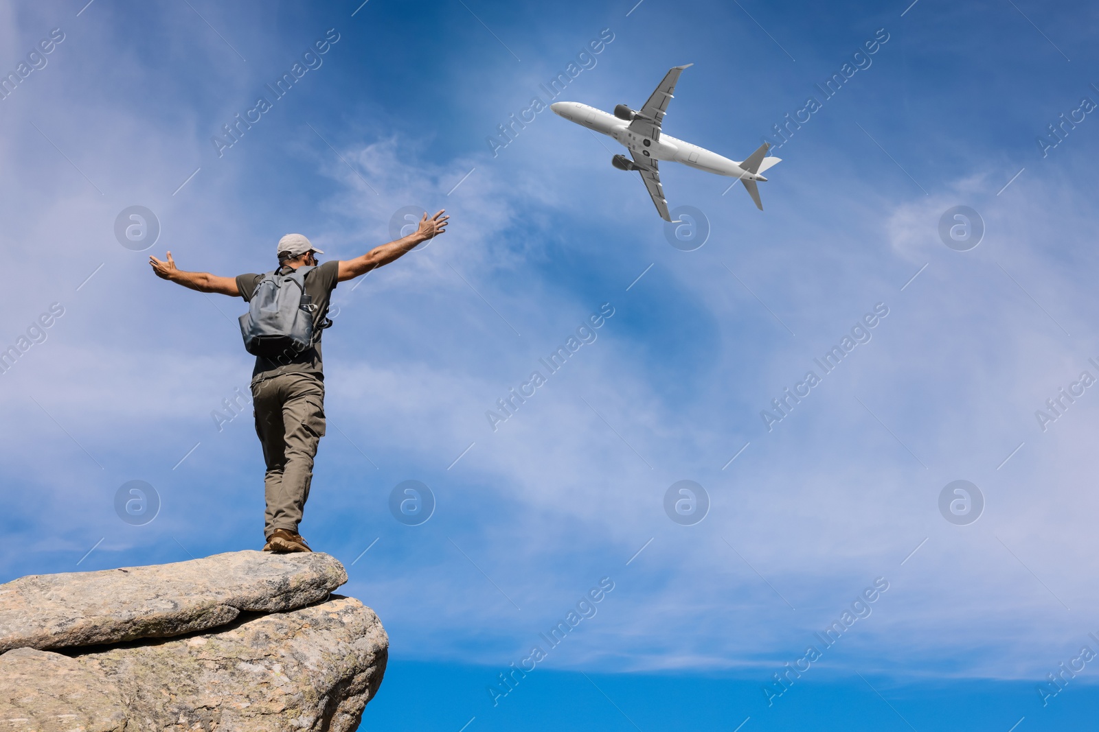 Image of Man on cliff looking at airplane flying in sky