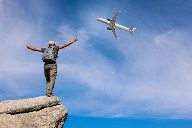 Man on cliff looking at airplane flying in sky