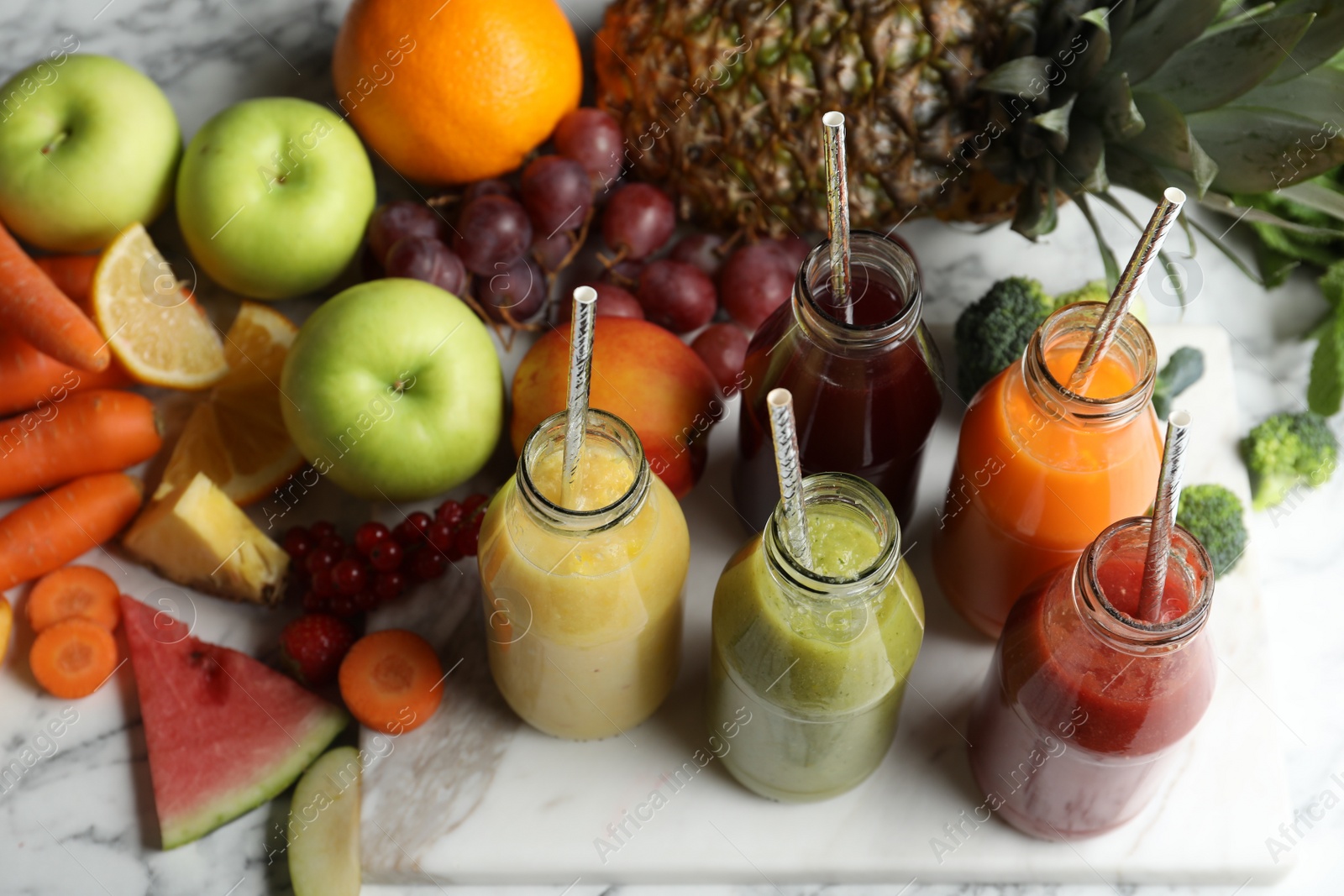 Photo of Bottles of delicious juices and fresh fruits on white marble table