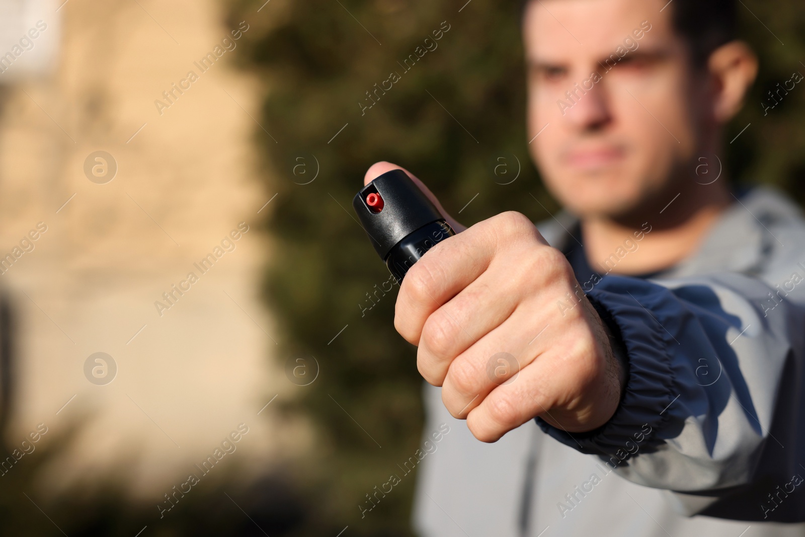 Photo of Man using pepper spray outdoors, focus on hand. Space for text