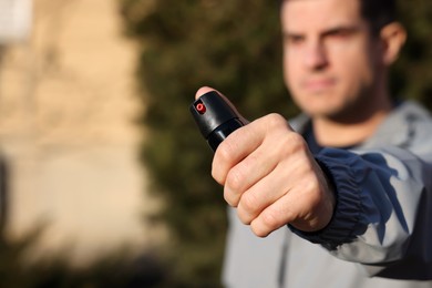 Man using pepper spray outdoors, focus on hand. Space for text