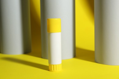 Glue stick near paper rolls on yellow background
