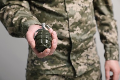 Photo of Soldier holding hand grenade on light grey background, closeup. Military service