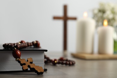 Photo of Bible, rosary beads, wooden cross and church candles on grey table, closeup. Space for text