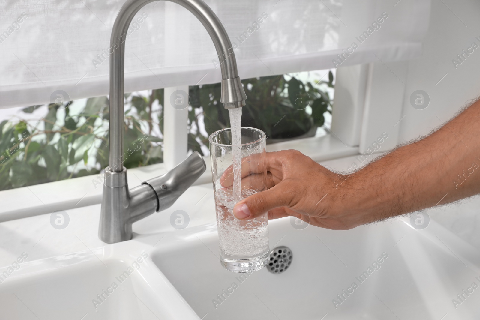 Photo of Man filling glass with water from tap at home, closeup