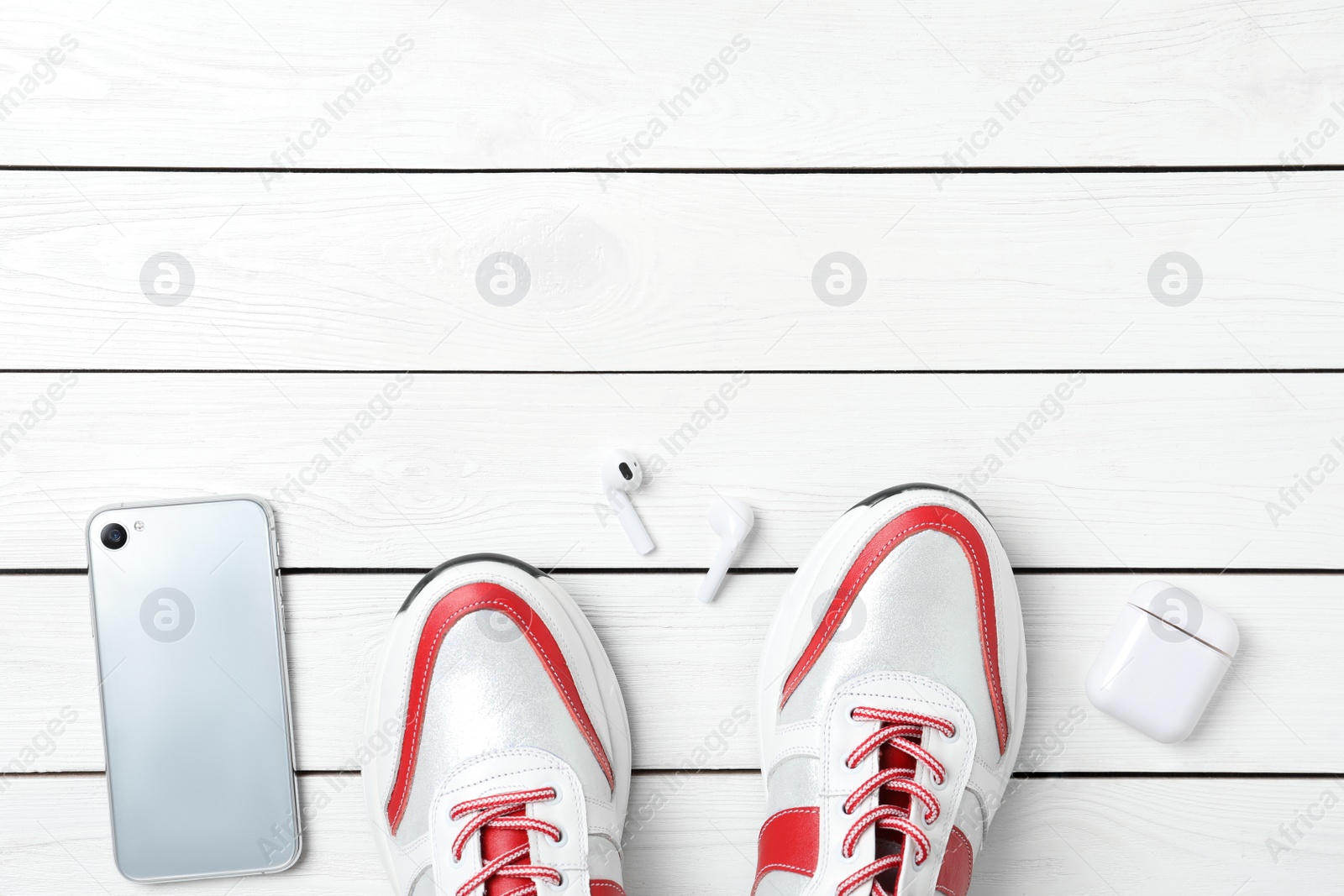 Photo of Pair of stylish shoes, modern smartphone and wireless earphones on white wooden table, flat lay. Space for text