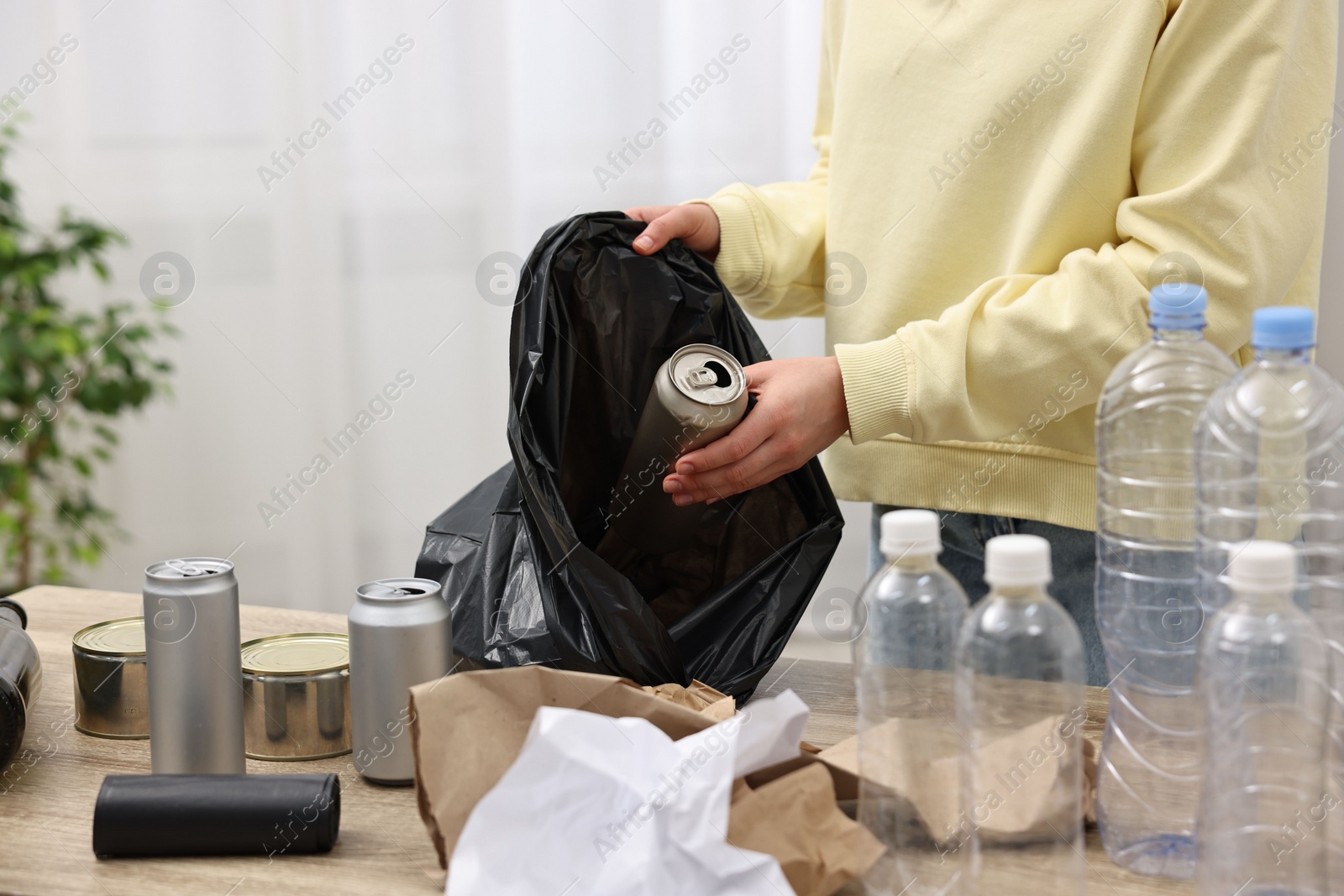 Photo of Woman separating garbage at table in room, closeup