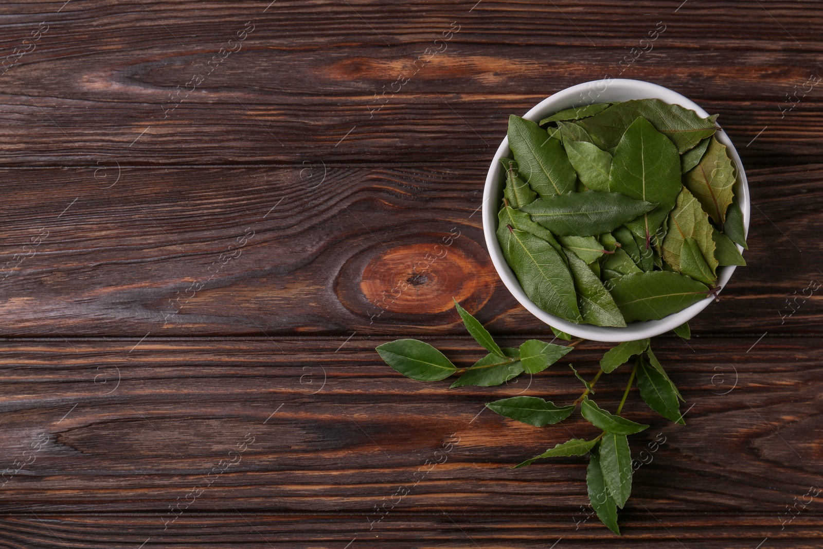 Photo of Fresh green bay leaves in bowl on wooden table, flat lay. Space for text