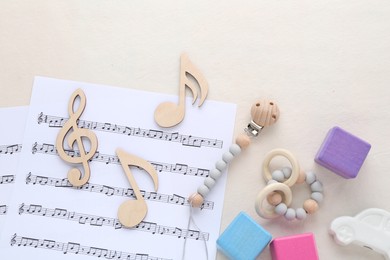 Photo of Wooden notes, music sheets and toys on beige background, flat lay. Baby song concept