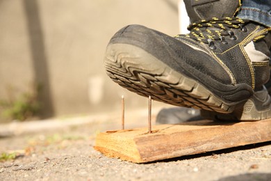 Photo of Careless worker stepping on nails in wooden plank outdoors, closeup. Space for text