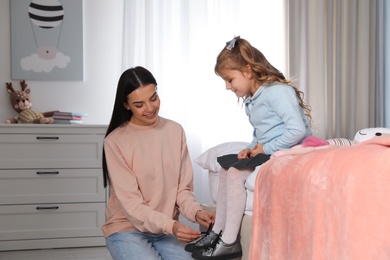 Young mother helping her little child get ready for school in bedroom