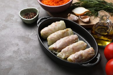 Photo of Uncooked stuffed cabbage rolls and ingredients on grey table. Space for text