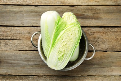 Whole and cut fresh Chinese cabbages in colander on wooden table, top view