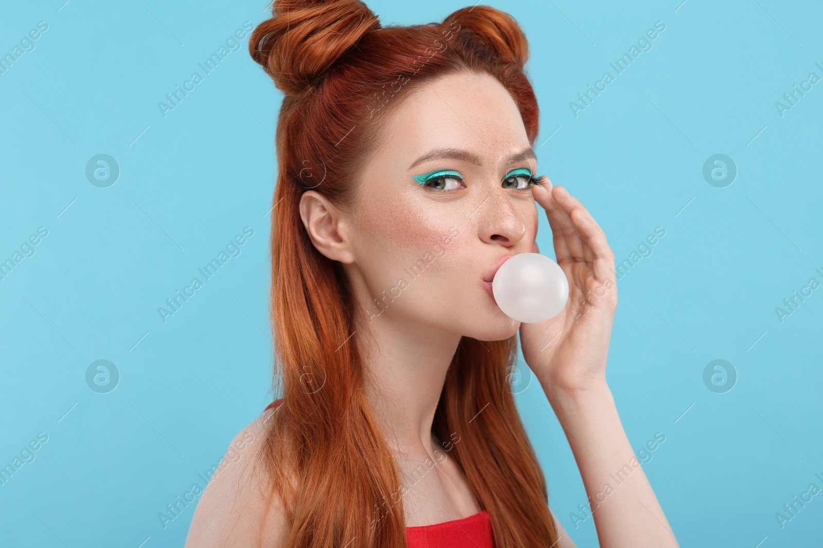 Photo of Portrait of beautiful woman with bright makeup blowing bubble gum on light blue background