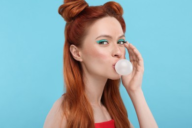 Photo of Portraitbeautiful woman with bright makeup blowing bubble gum on light blue background