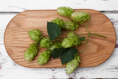 Photo of Board with branch of fresh hops on white wooden table, top view