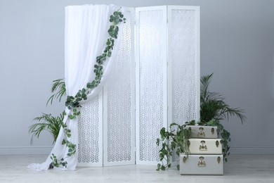 Photo of Stylish photo zone with white folding screen, floral decor and vintage suitcases indoors