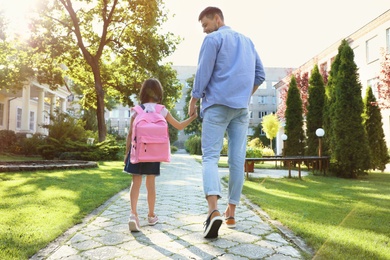 Photo of Father taking his little child to school through park
