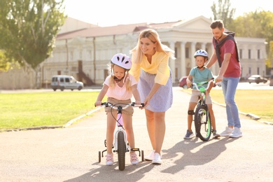 Happy parents teaching children to ride bicycles outdoors