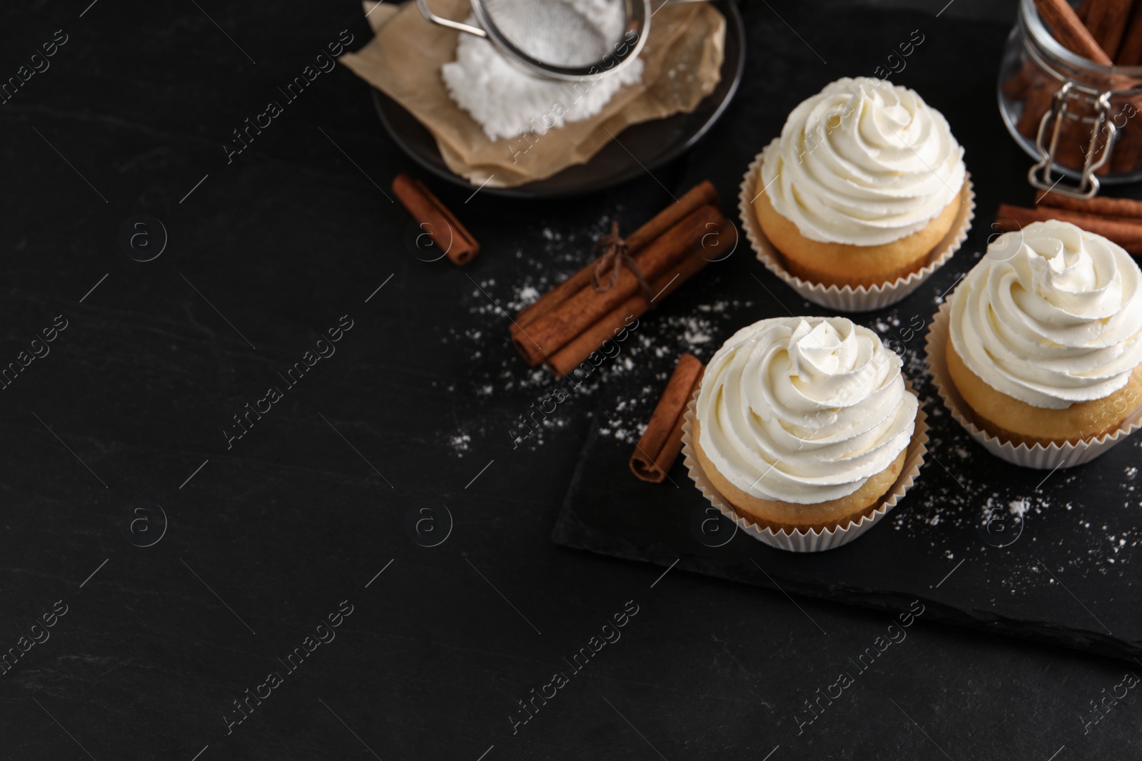 Photo of Delicious cupcakes with cream and cinnamon on black table. Space for text