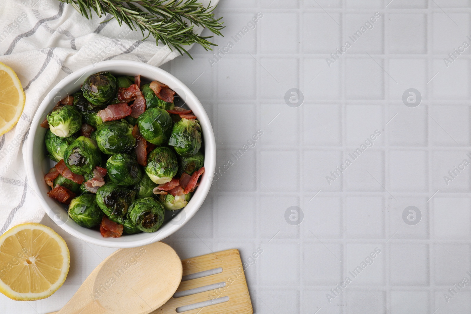 Photo of Delicious roasted Brussels sprouts and bacon served on white tiled table, flat lay. Space for text