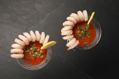 Tasty shrimp cocktail with sauce in glasses and lemon on grey textured table, flat lay