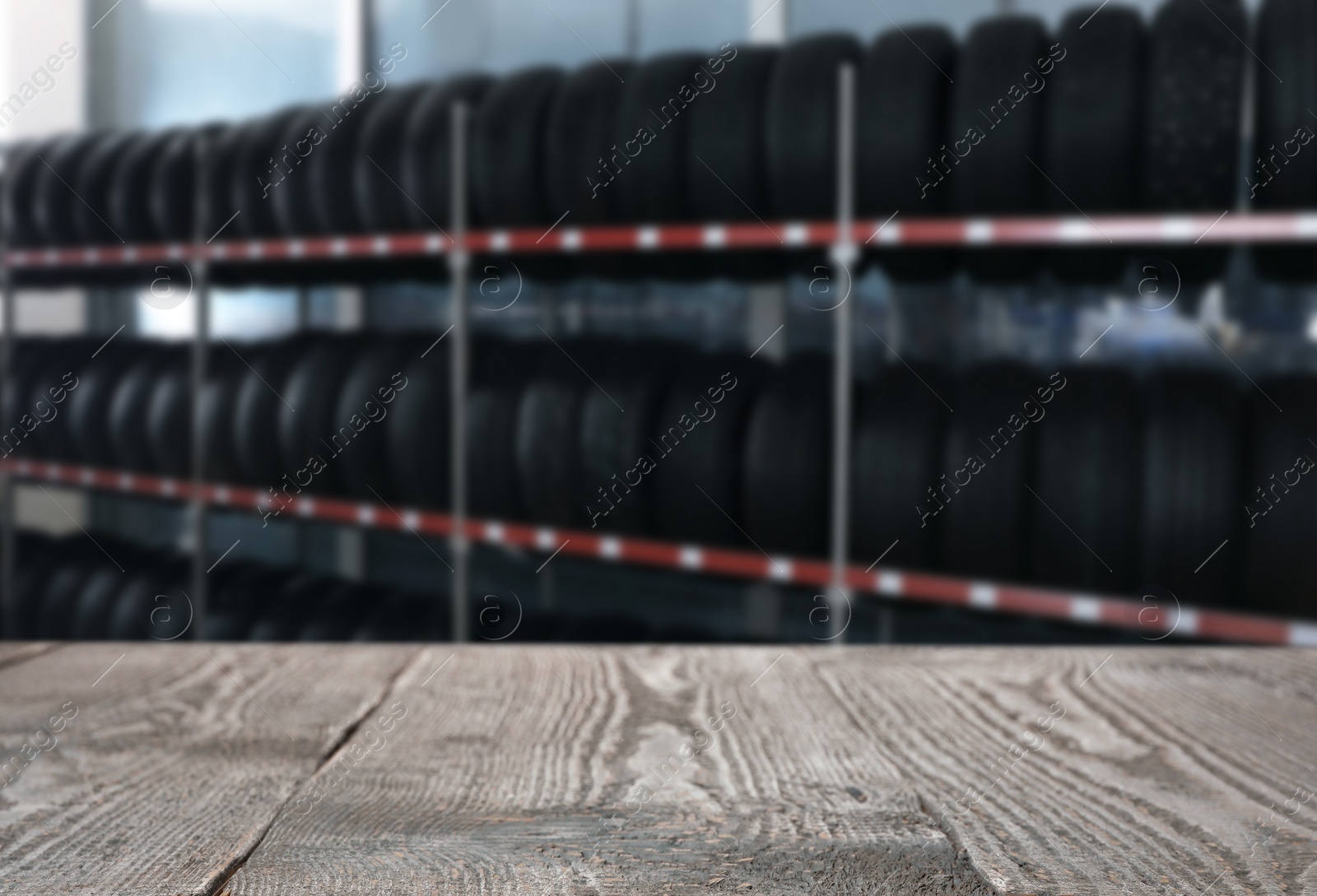 Image of Empty wooden surface and blurred view of car tires in auto store, closeup. Space for text 