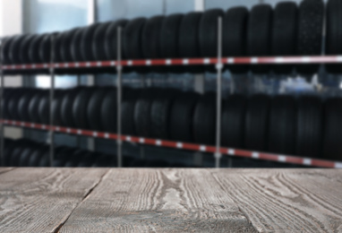 Image of Empty wooden surface and blurred view of car tires in auto store, closeup. Space for text 