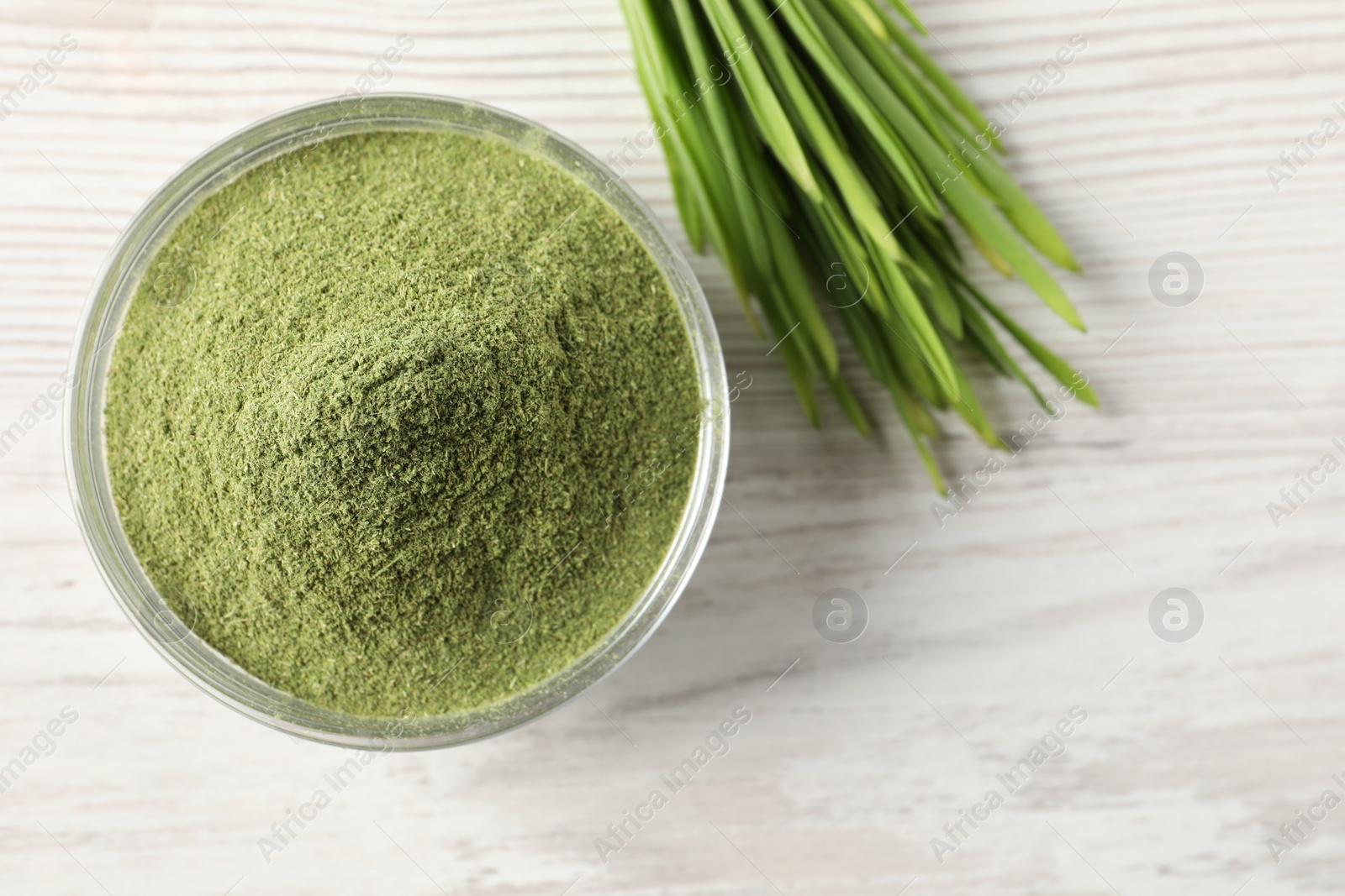 Photo of Wheat grass powder in bowl and fresh sprouts on white wooden table, flat lay. Space for text