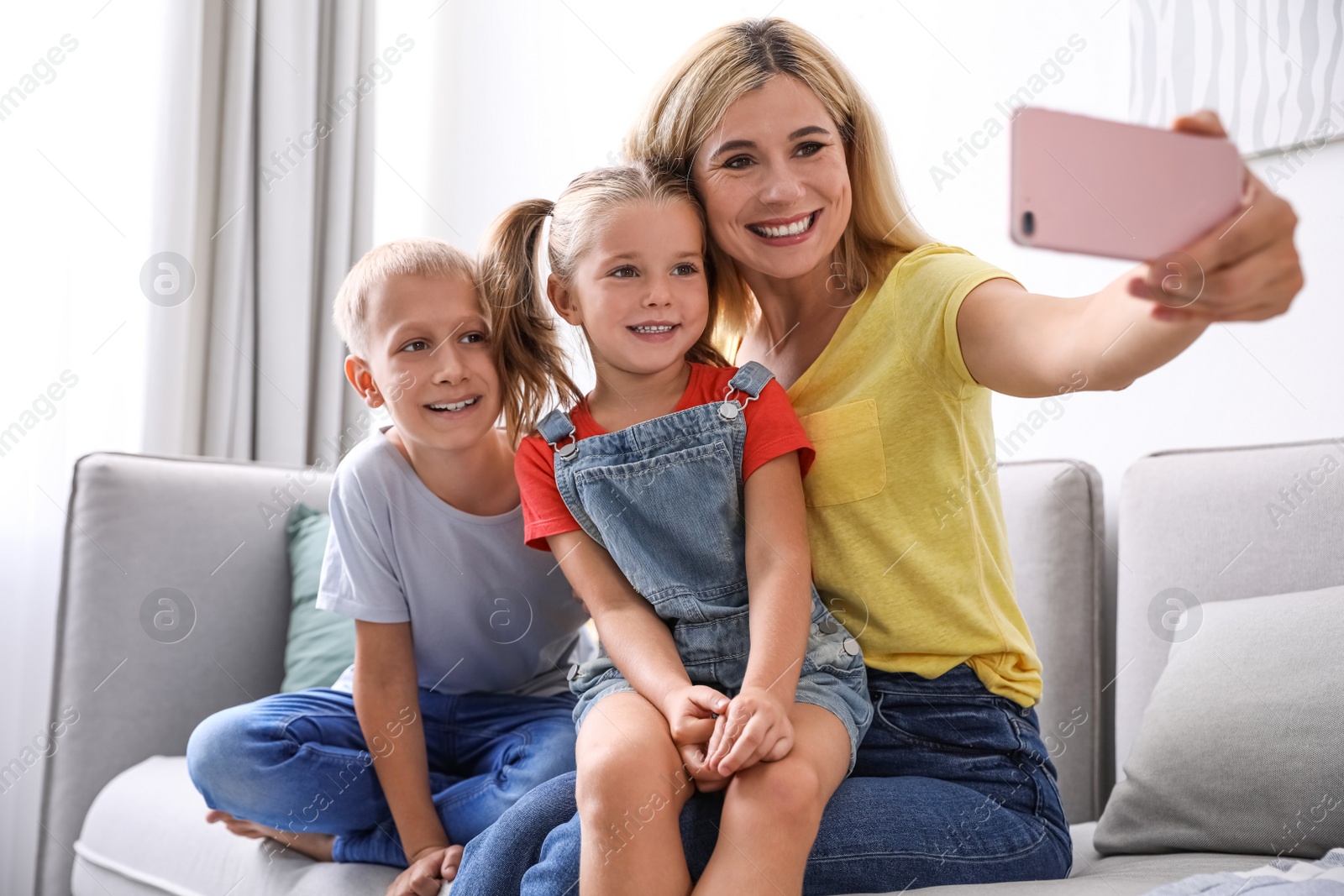 Photo of Happy mother taking selfie with her children on sofa at home
