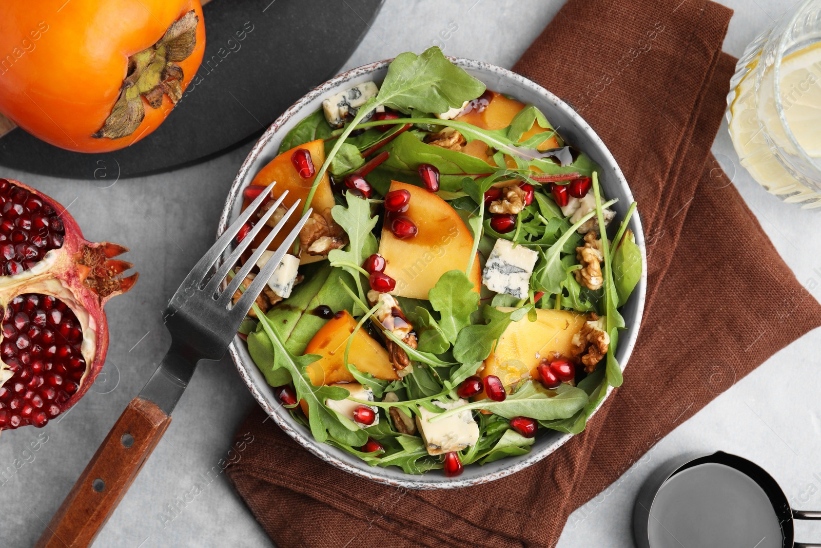 Photo of Tasty salad with persimmon, blue cheese, pomegranate and walnuts served on light grey table, flat lay