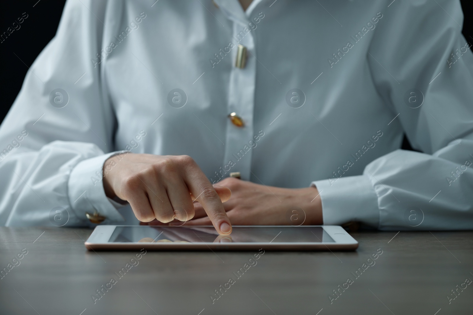 Photo of Closeup view of woman using modern tablet at table on dark background