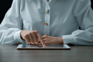 Closeup view of woman using modern tablet at table on dark background