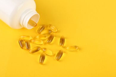 White medical bottle and vitamin capsules on yellow background, above view. Space for text