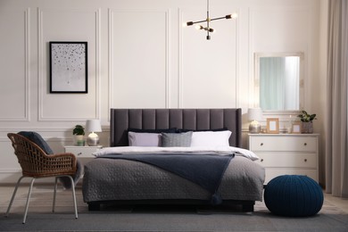 Stylish bedroom interior with large comfortable bed, chair and chest of drawers