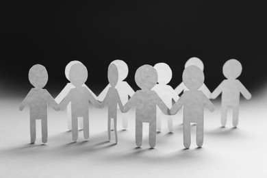 Photo of Teamwork concept. Paper figures of people holding hands on white table, closeup