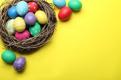 Bright painted eggs in nest on yellow background, flat lay with space for text. Happy Easter