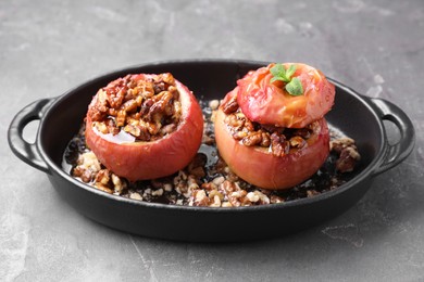 Photo of Tasty baked apples with nuts, honey and mint in baking dish on gray textured table