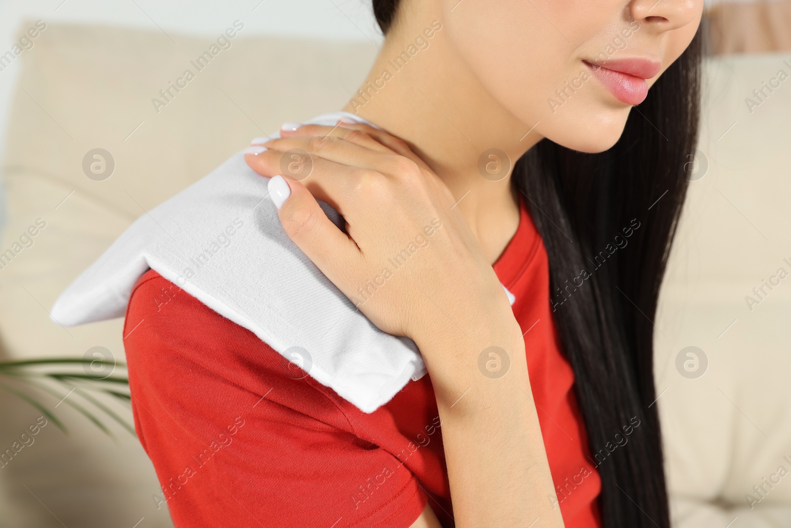 Photo of Young woman using heating pad at home, closeup