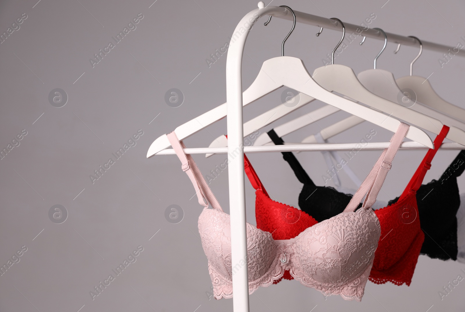 Photo of Hangers with beautiful lace bras on rack against grey background. Stylish underwear