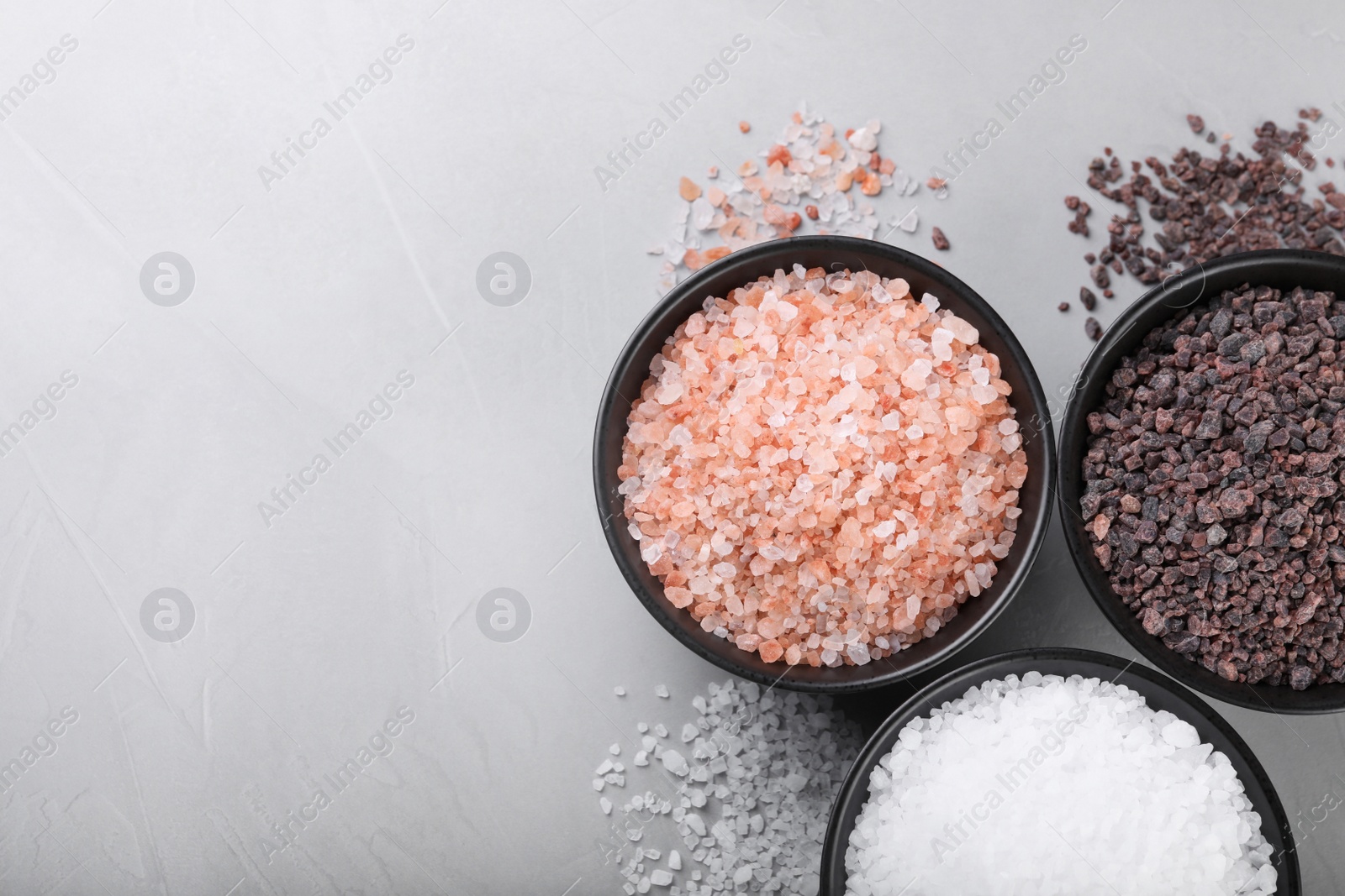 Photo of Different kinds of salt on light grey marble table, flat lay. Space for text