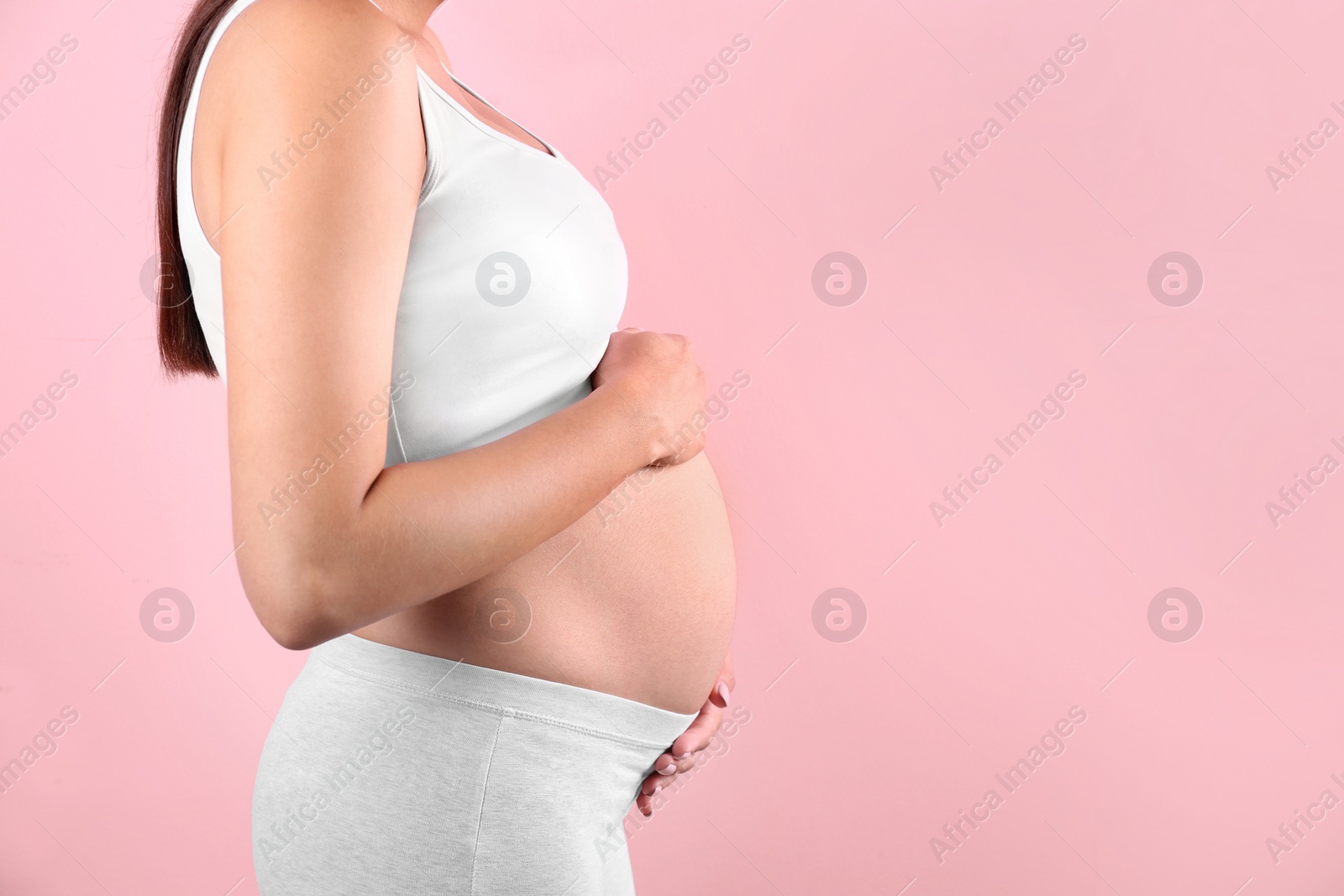 Photo of Young pregnant woman holding hands on belly against color background, closeup. Space for text